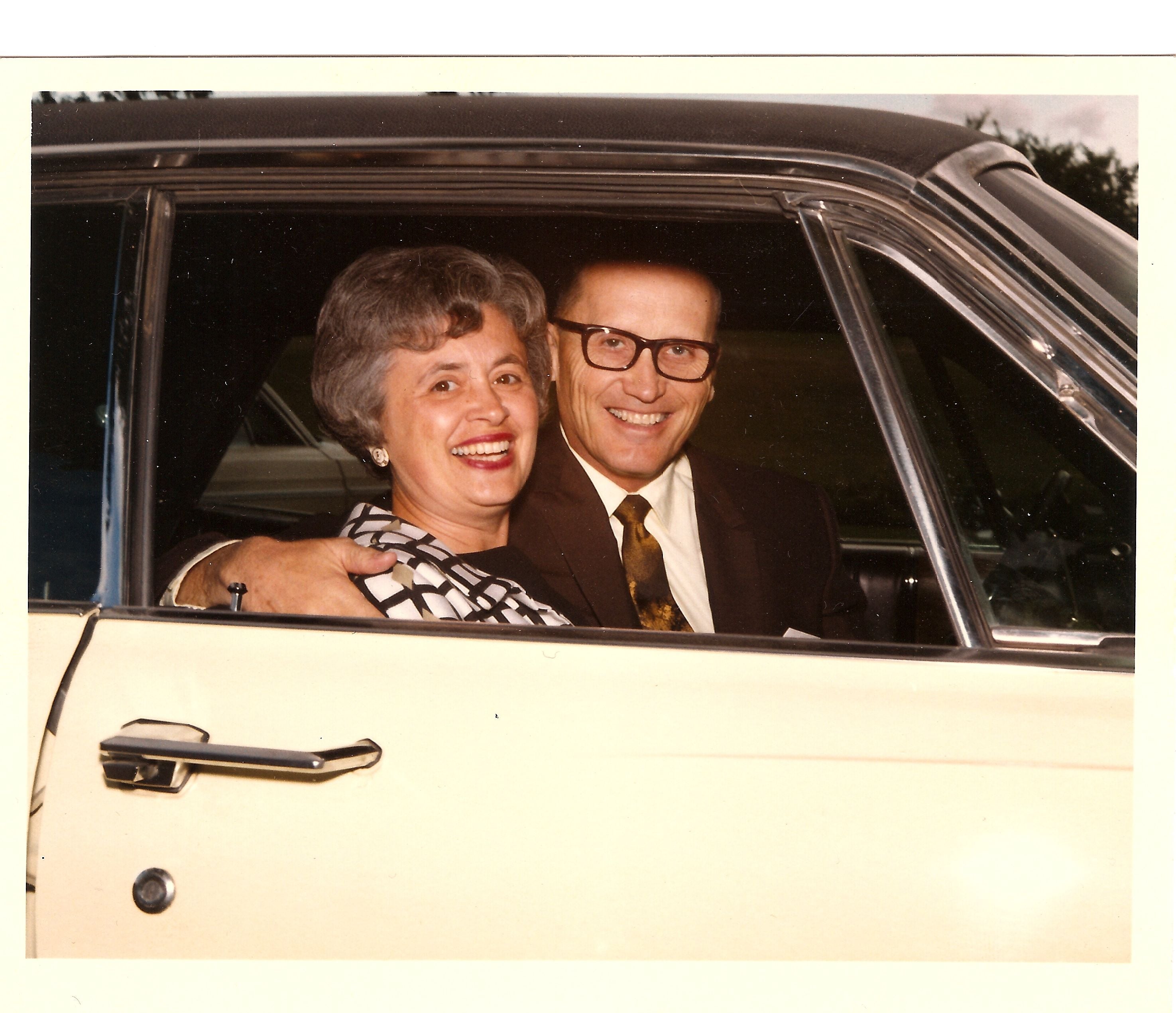 Smiling man and woman looking out from a car window.