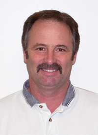 Smiling man with brown hair and a mustache in a white collared shirt.
